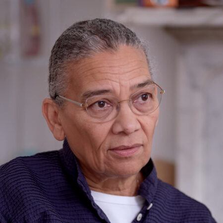 A person with short gray hair and glasses, wearing a dark textured shirt.