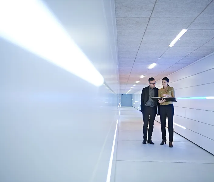 Two colleagues walk down an office hallway while conversing